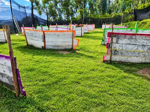 Campo de Tablas de Quito Woodsball: barricadas de madera pintadas en colores sobre césped, rodeadas de mallas y bosque