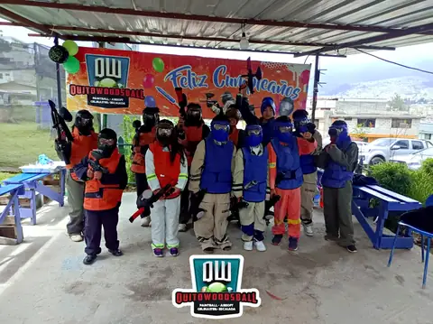 Cumpleaños infantil: niños con equipo de paintball bajo el letrero de Feliz Cumpleaños