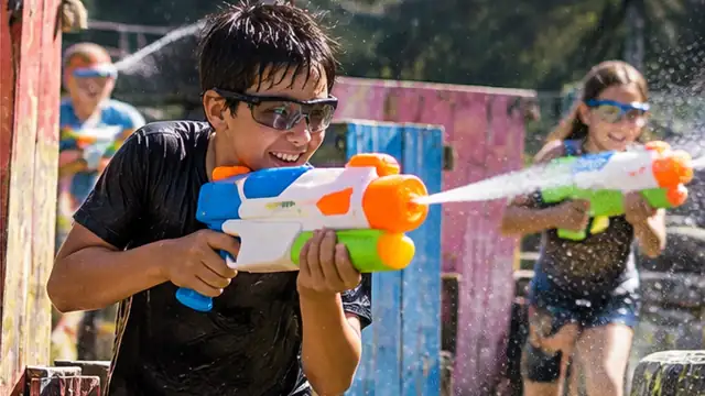 Niños jugando con pistolas de agua y gafas de protección entre barricadas de colores